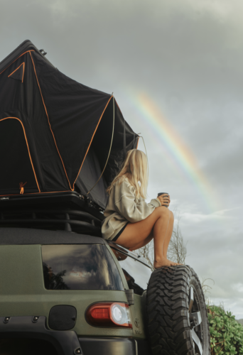 woman sighting rainbow while sitting on camper