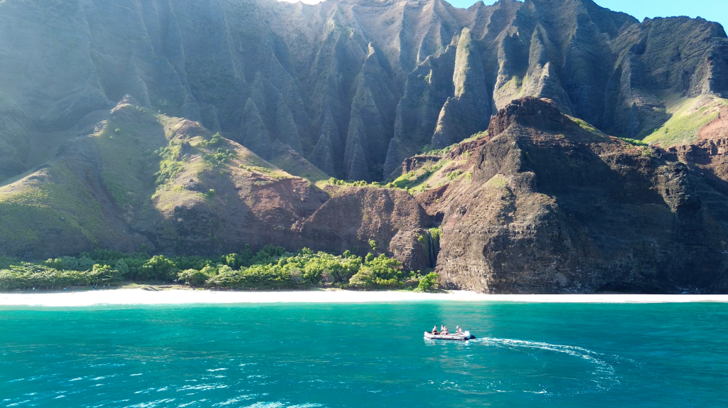 A rigid inflatable boat (RIB) with four passengers is cruising along the Nā Pali Coast in Kauai, Hawaii.